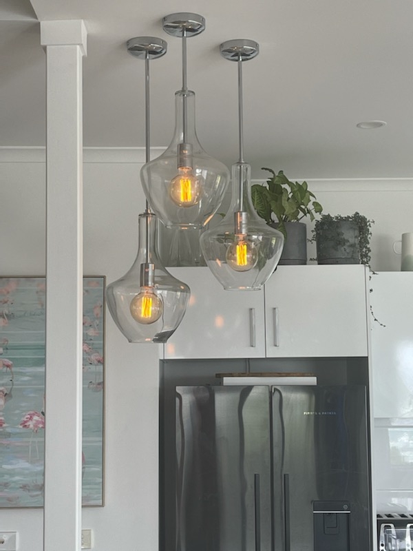 Three glass pendant lights with warm filament bulbs above a kitchen bench