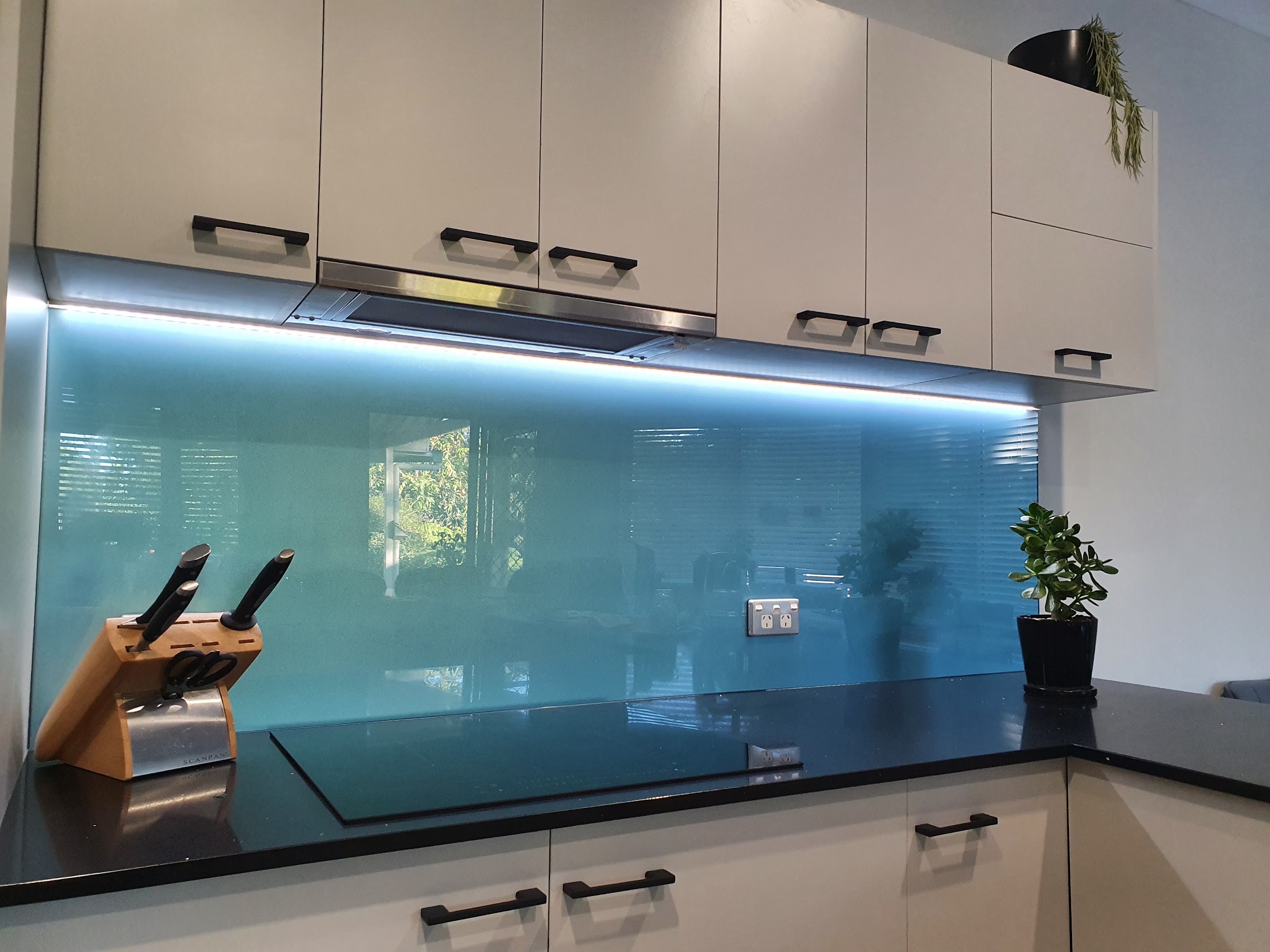 LED strip lighting under a rangehood above a teal glass splashback